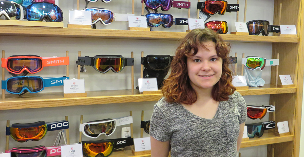 cydney standing in front of a wall of goggles at saint bernard sports