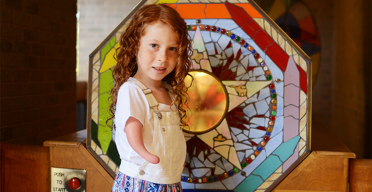 young girl with red hair standing in front of stained glass