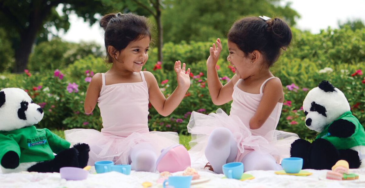 Twins with hand disorders play in the grass dressed as ballerinas